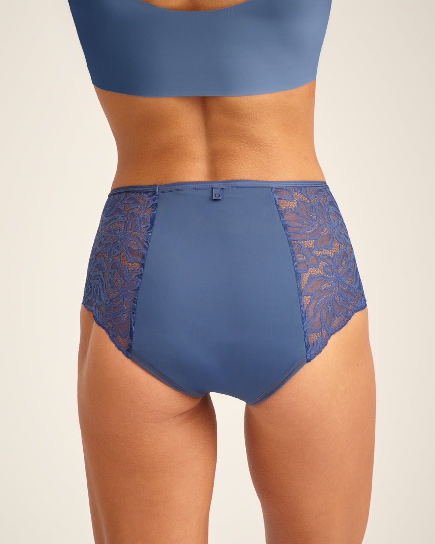 Modell trägt ooia Highwaist Lace Extra Strong in Smoky Blue – elegante Periodenunterwäsche mit hohem Spitzenbund und Spitzeneinsätzen. Rückansicht.