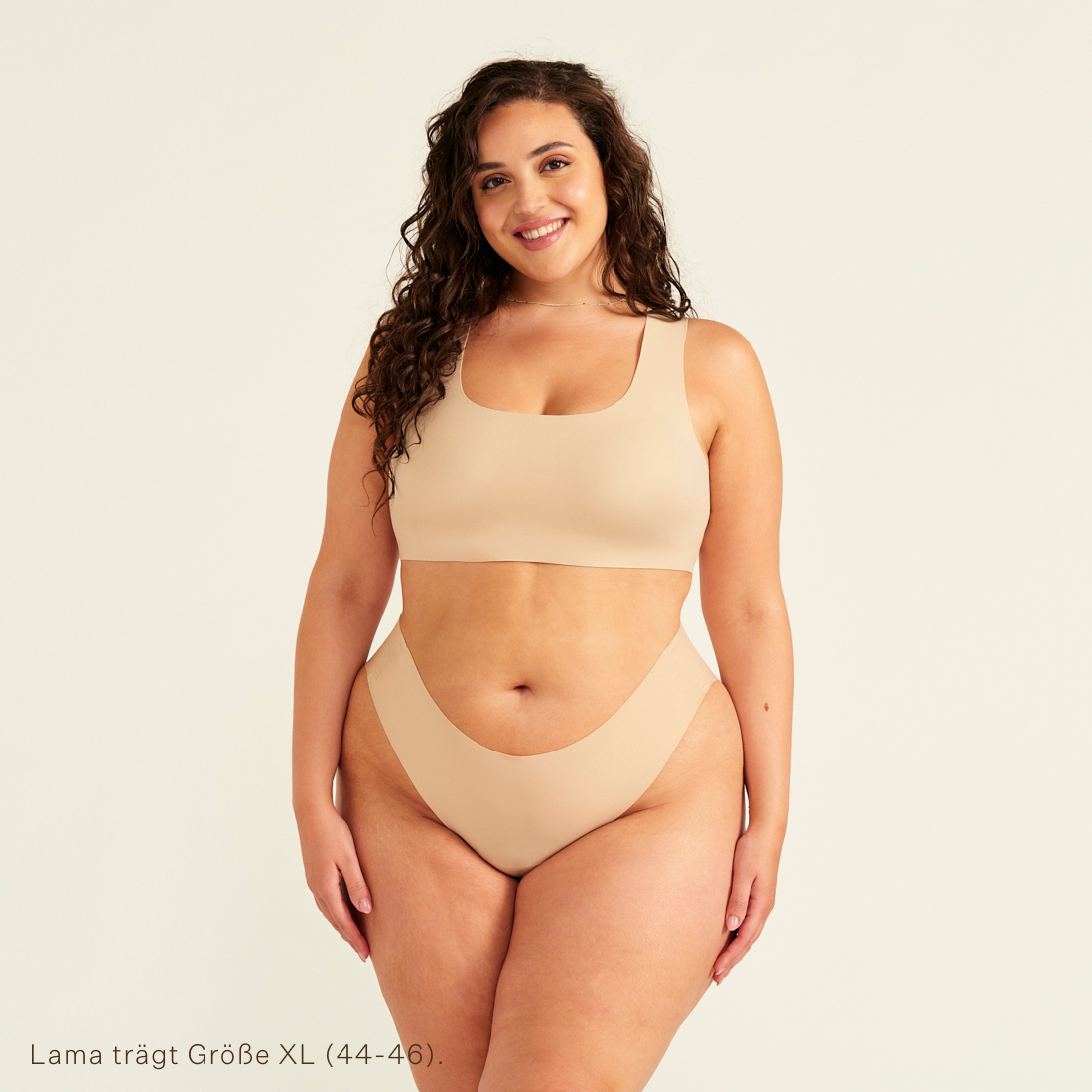Modell trägt ooia All-You-Need Bra Top in XL in Beige – bügelloses, nahtloses Bustier mit breiten Trägern, dazu passed Periodenslip Seamless in Beige.