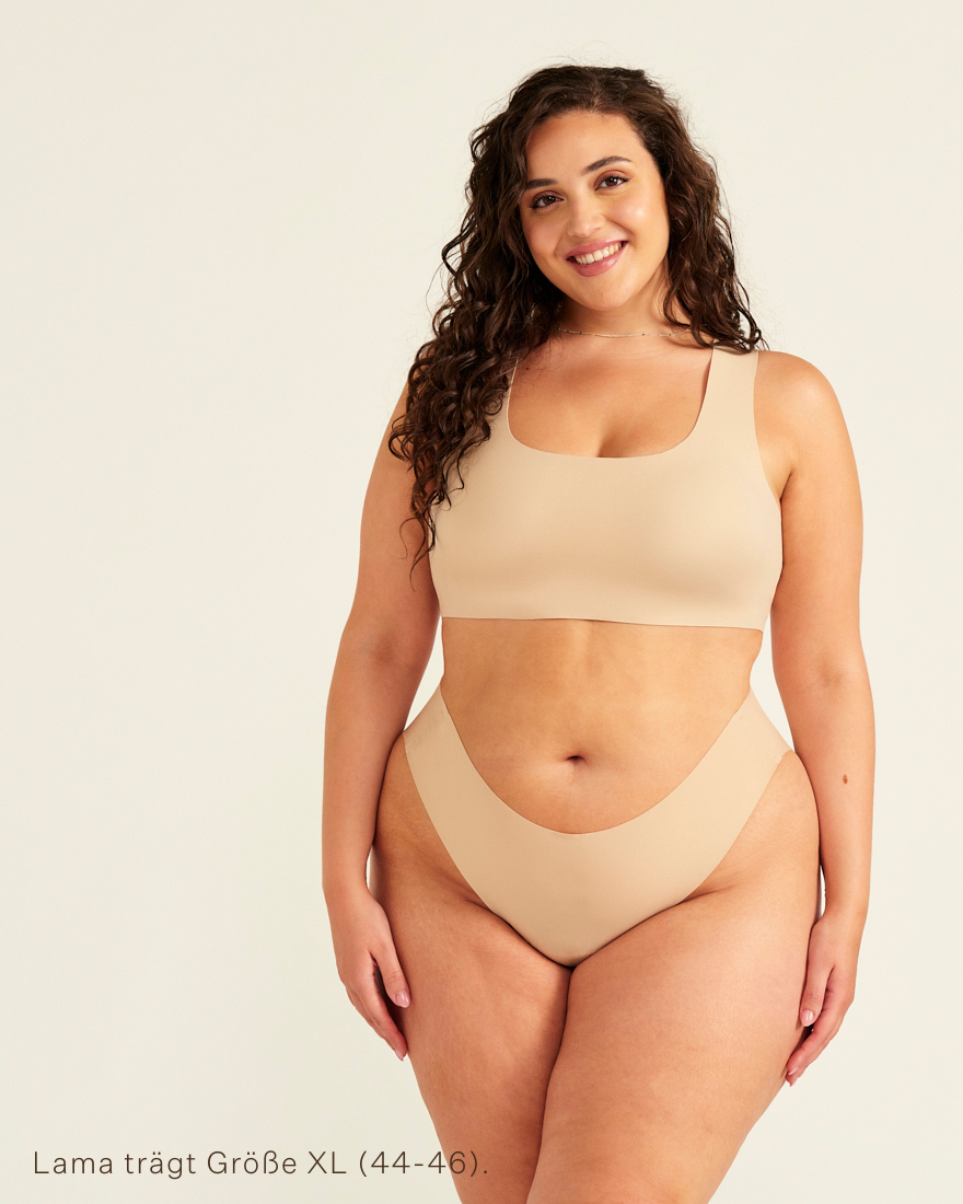 Modell trägt ooia All-You-Need Bra Top in XL in Beige – bügelloses, nahtloses Bustier mit breiten Trägern, dazu passed Periodenslip Seamless in Beige.