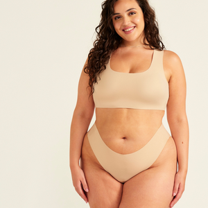 Modell trägt ooia All-You-Need Bra Top in XL in Beige – bügelloses, nahtloses Bustier mit breiten Trägern, dazu passed Periodenslip Seamless in Beige.
