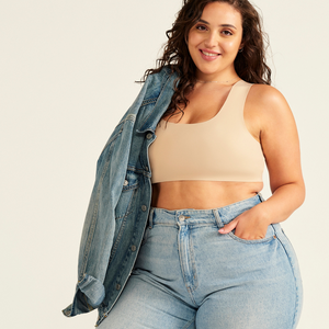Modell trägt ooia All-You-Need Bra Top in XL in Beige – bügelloses, nahtloses Bustier mit breiten Trägern, als Top zu Jeans und Jacke.