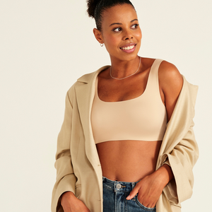 Modell trägt ooia All-You-Need Bra Top in XL in Beige – bügelloses, nahtloses Bustier mit breiten Trägern, als Top zu Jeans und Jacke.