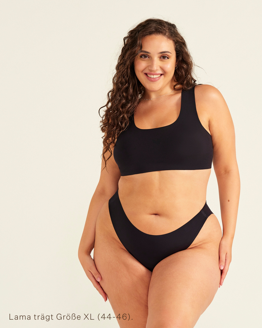 Modell trägt ooia All-You-Need Bra Top in Größe XL in Schwarz – bügelloses, nahtloses Bustier mit breiten Trägern, dazu ooia Periodenslip Seamless schwarz.