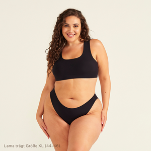 Modell trägt ooia All-You-Need Bra Top in Größe XL in Schwarz – bügelloses, nahtloses Bustier mit breiten Trägern, dazu ooia Periodenslip Seamless schwarz.