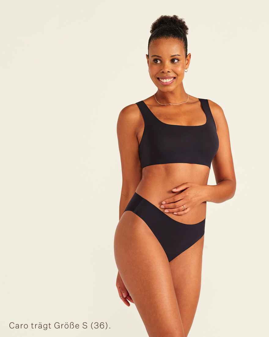 Modell trägt ooia All-You-Need Bra Top in Größe S in Schwarz – bügelloses, nahtloses Bustier mit breiten Trägern, dazu ooia Periodenslip Seamless schwarz.