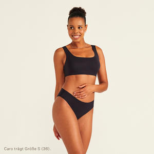 Modell trägt ooia All-You-Need Bra Top in Größe S in Schwarz – bügelloses, nahtloses Bustier mit breiten Trägern, dazu ooia Periodenslip Seamless schwarz.