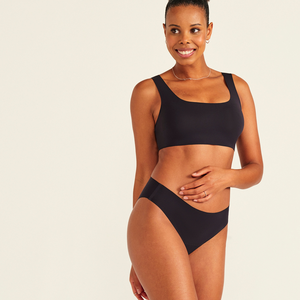 Modell trägt ooia All-You-Need Bra Top in Größe S in Schwarz – bügelloses, nahtloses Bustier mit breiten Trägern, dazu ooia Periodenslip Seamless schwarz.