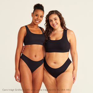 Zwei Models unterschiedlicher Konfektion tragen ooia All-You-Need Bra Top in Schwarz – bügelloses, nahtloses Bustier mit breiten Trägern, dazu ooia Periodenslip Seamless schwarz.