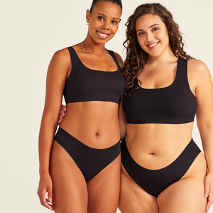 Zwei Models unterschiedlicher Konfektion tragen ooia All-You-Need Bra Top in Schwarz – bügelloses, nahtloses Bustier mit breiten Trägern, dazu ooia Periodenslip Seamless schwarz.