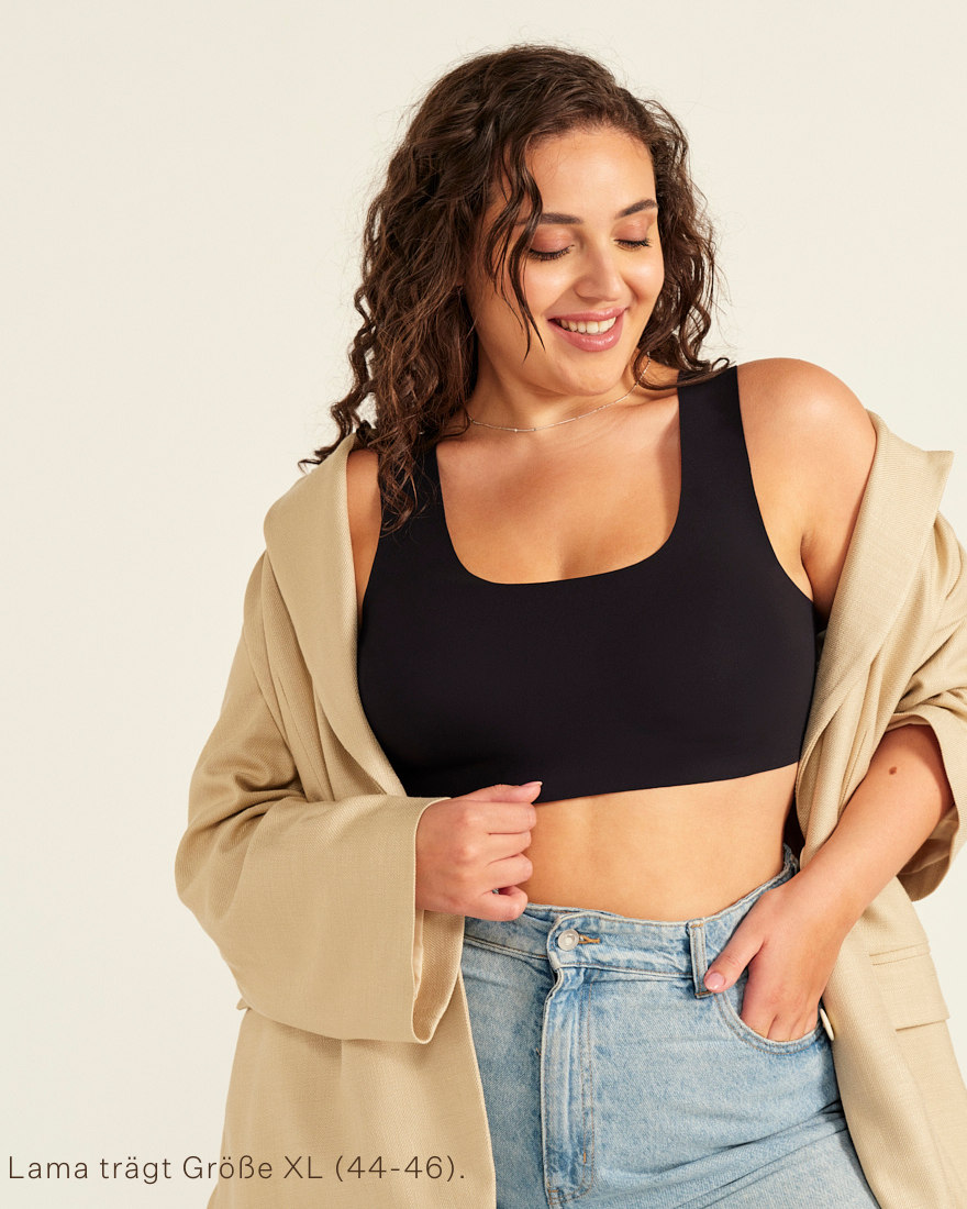Modell trägt ooia All-You-Need Bra Top in Schwarz – bügelloses, nahtloses Bustier mit breiten Trägern, dazu Jacke und Jeans.