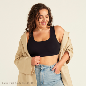 Modell trägt ooia All-You-Need Bra Top in Schwarz – bügelloses, nahtloses Bustier mit breiten Trägern, dazu Jacke und Jeans.