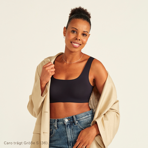 Modell trägt ooia All-You-Need Bra Top in Schwarz – bügelloses, nahtloses Bustier mit breiten Trägern, dazu Jacke und Jeans.