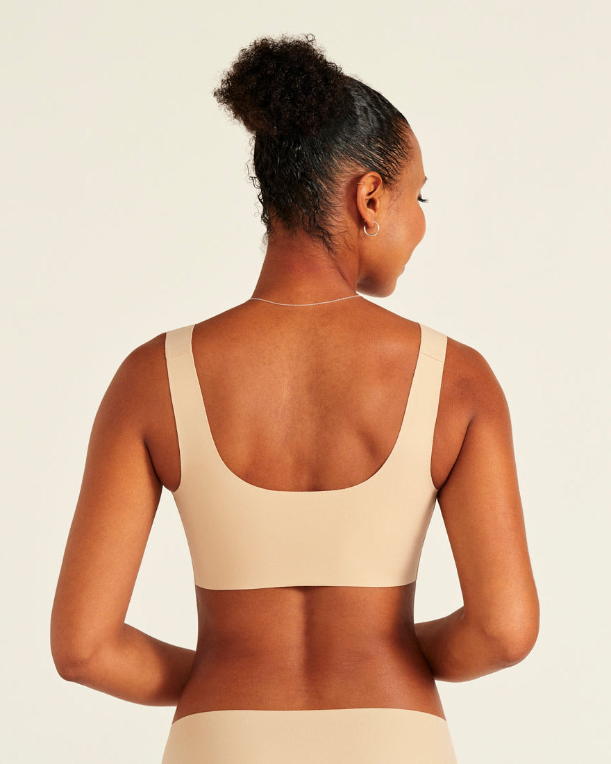Modell trägt ooia All-You-Need Bra Top in Beige – bügelloses, nahtloses Bustier mit breiten Trägern. Rückansicht.