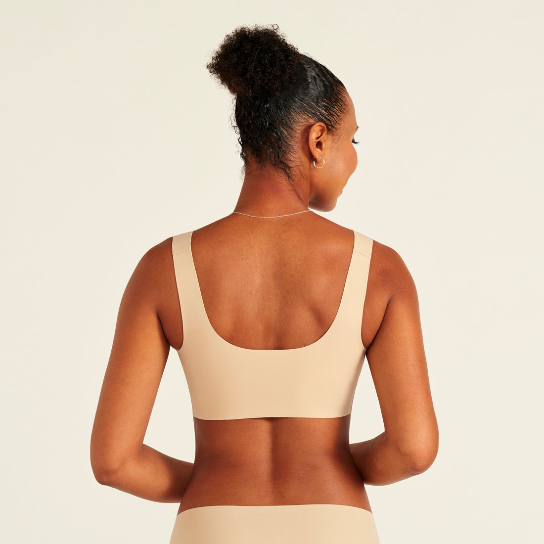 Modell trägt ooia All-You-Need Bra Top in Beige – bügelloses, nahtloses Bustier mit breiten Trägern. Rückansicht.
