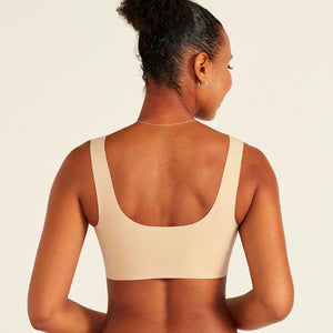 Modell trägt ooia All-You-Need Bra Top in Beige – bügelloses, nahtloses Bustier mit breiten Trägern. Rückansicht.