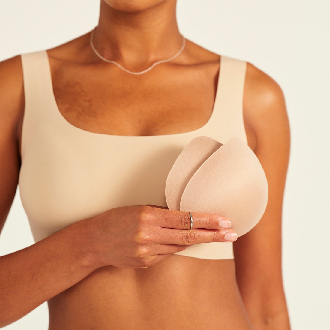 Modell trägt ooia All-You-Need Bra Top in Beige – bügelloses, nahtloses Bustier mit breiten Trägern. Model hält herausgenommene Pads.