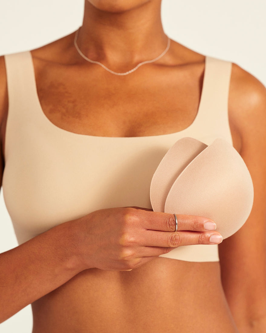 Modell trägt ooia All-You-Need Bra Top in Beige – bügelloses, nahtloses Bustier mit breiten Trägern. Model hält herausgenommene Pads.
