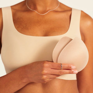 Modell trägt ooia All-You-Need Bra Top in Beige – bügelloses, nahtloses Bustier mit breiten Trägern. Model hält herausgenommene Pads.
