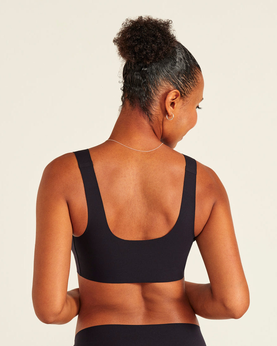 Modell trägt ooia All-You-Need Bra Top in Schwarz – bügelloses, nahtloses Bustier mit breiten Trägern. Rückansicht.