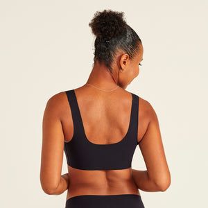 Modell trägt ooia All-You-Need Bra Top in Schwarz – bügelloses, nahtloses Bustier mit breiten Trägern. Rückansicht.