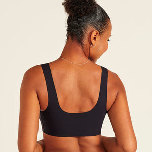 Modell trägt ooia All-You-Need Bra Top in Schwarz – bügelloses, nahtloses Bustier mit breiten Trägern. Rückansicht.