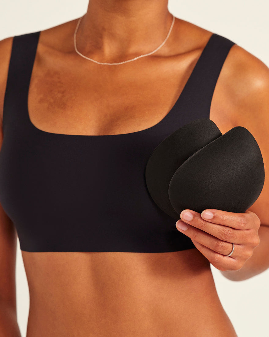 Modell trägt ooia All-You-Need Bra Top in Schwarz – bügelloses, nahtloses Bustier mit breiten Trägern. Model hält herausnehmbare Pads.