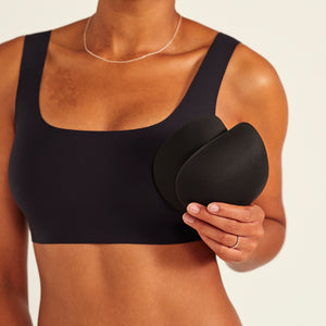 Modell trägt ooia All-You-Need Bra Top in Schwarz – bügelloses, nahtloses Bustier mit breiten Trägern. Model hält herausnehmbare Pads.