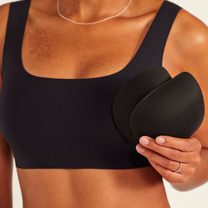Modell trägt ooia All-You-Need Bra Top in Schwarz – bügelloses, nahtloses Bustier mit breiten Trägern. Model hält herausnehmbare Pads.