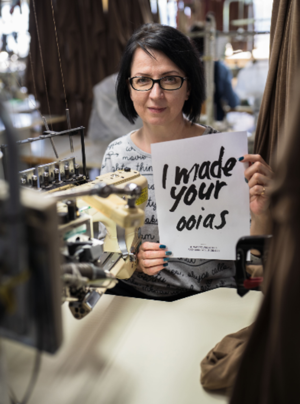 Frau hält Schild "Who made your ooias". Sitzend und frontal.