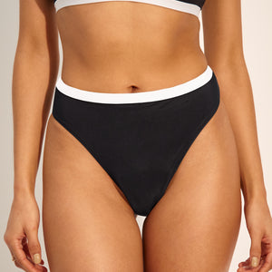 Modell trägt ooia Perioden Beachwear Slip in schwarz mit weißen Kontrastdetails.
frontal nah