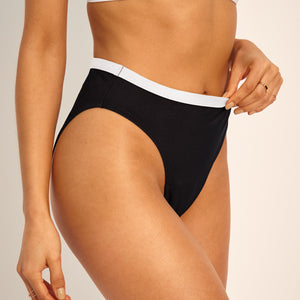 Modell trägt ooia Perioden Beachwear Slip in schwarz mit weißen Kontrastdetails.
seitlich