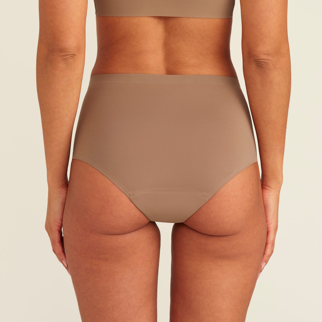 Modell trägt ooia Periodenunterwäsche Highwaist Seamless in Taupe mit hohem Bund und nahtlosem Design, Rückansicht