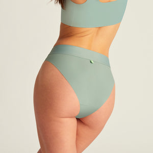 Modell trägt ooia Slip Seamless Cheeky in Sage – nahtlose Periodenunterwäsche mit hohem Beinausschnitt. Rückansicht.
