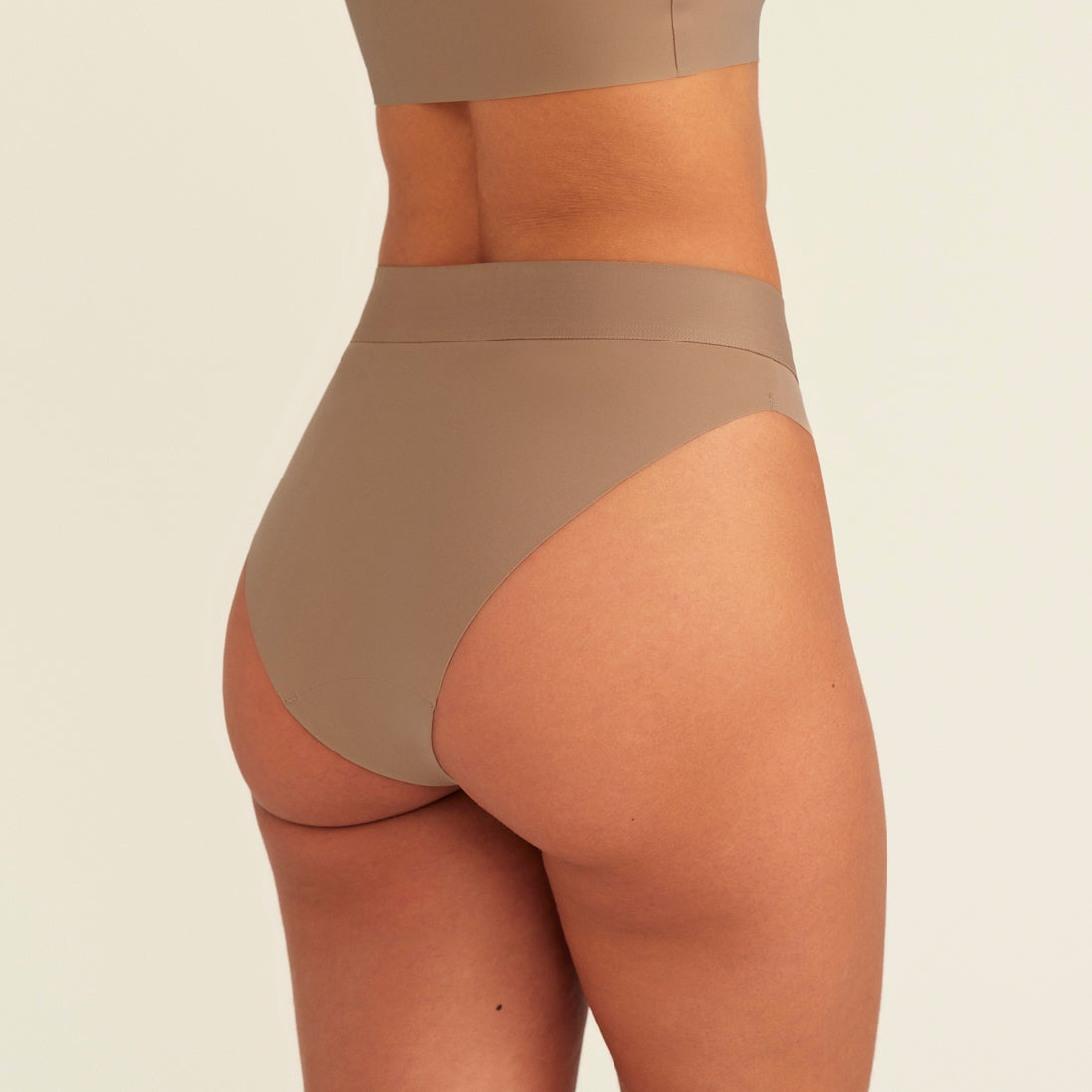 Modell trägt ooia Periodenslip Seamless Cheeky in Taupe mit hohem Beinausschnitt, Rückansicht
