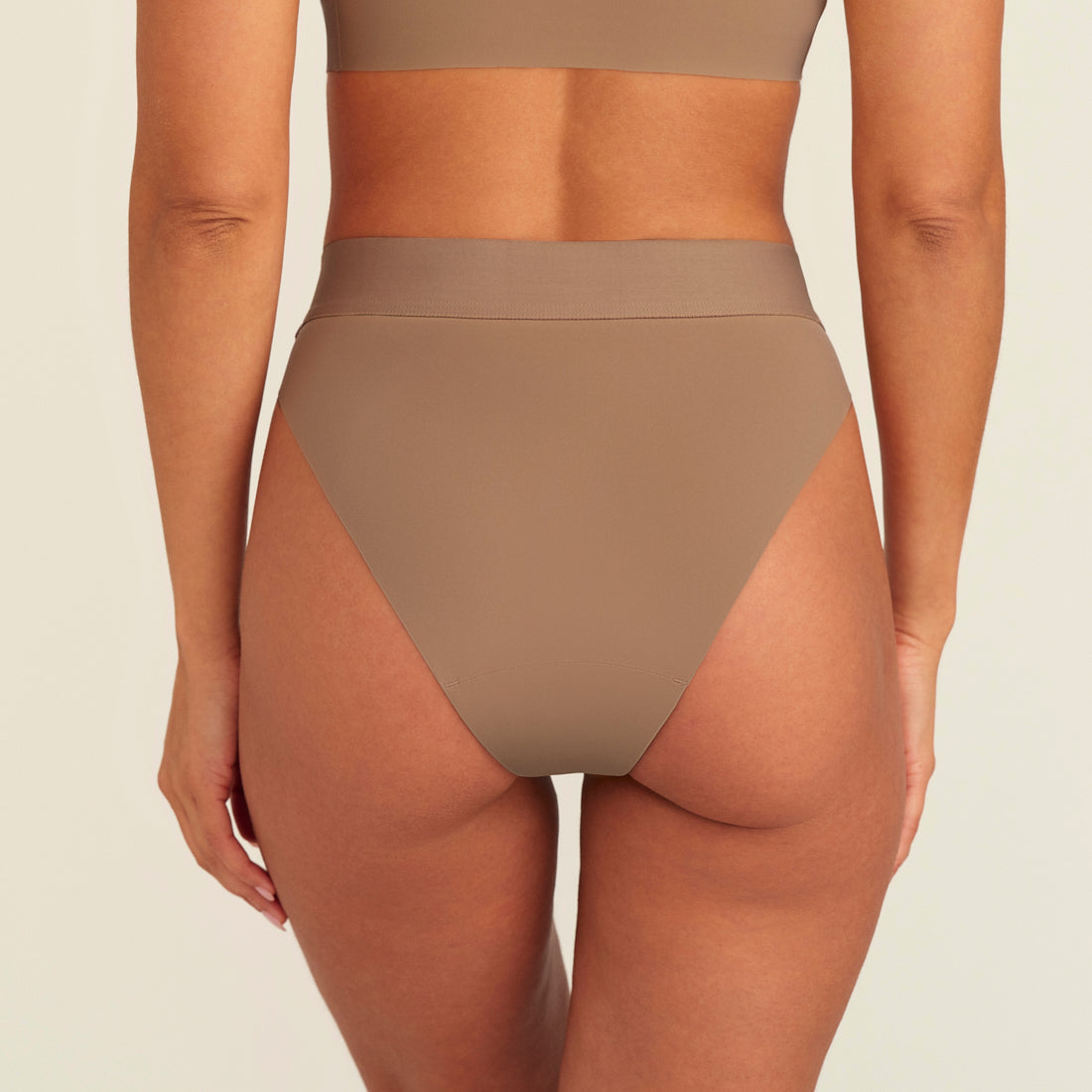 Modell trägt ooia Periodenslip Seamless Cheeky in Taupe mit hohem Beinausschnitt, Rückansicht