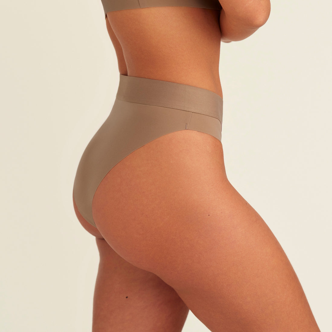 Modell trägt ooia Periodenslip Seamless Cheeky in Taupe mit hohem Beinausschnitt