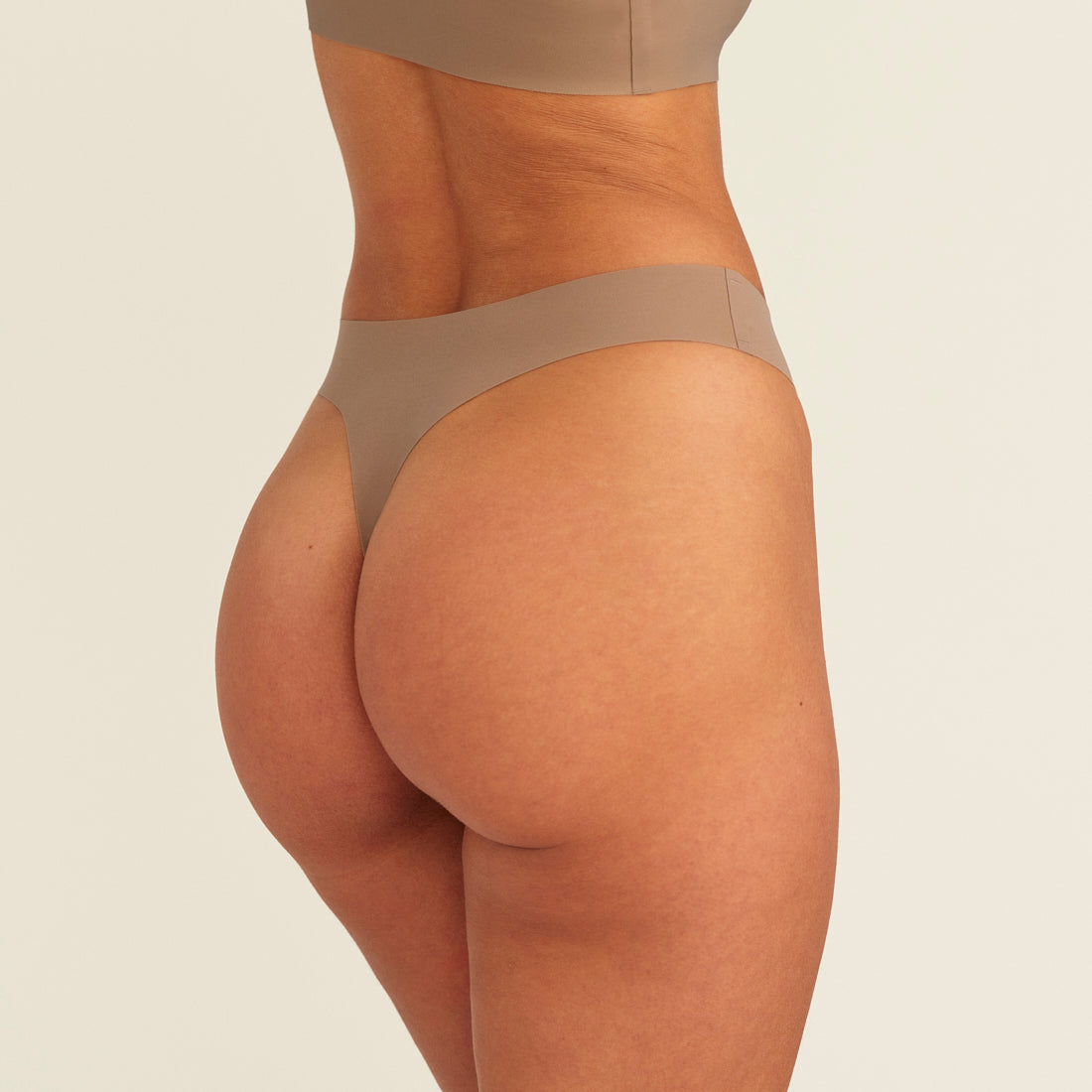 Modell trägt ooia Periodenunterwäsche String Seamless in Taupe mit leichter Saugstärke, Rückansicht