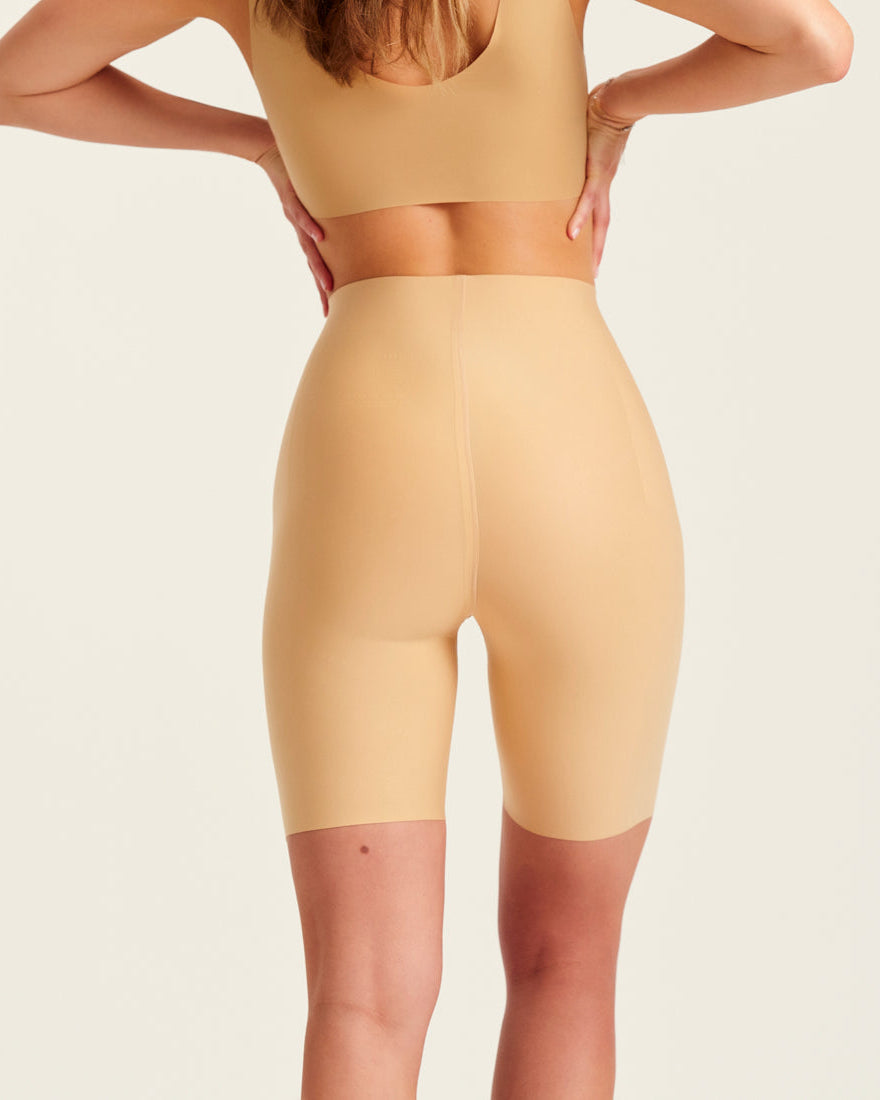 Modell trägt ooia Shape Short Thigh Saving in Beige – figurformende Short mit Oberschenkelschutz. Rückansicht.