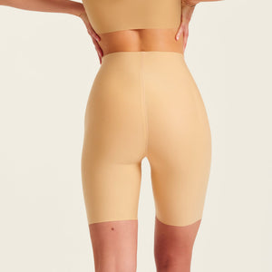 Modell trägt ooia Shape Short Thigh Saving in Beige – figurformende Short mit Oberschenkelschutz. Rückansicht.
