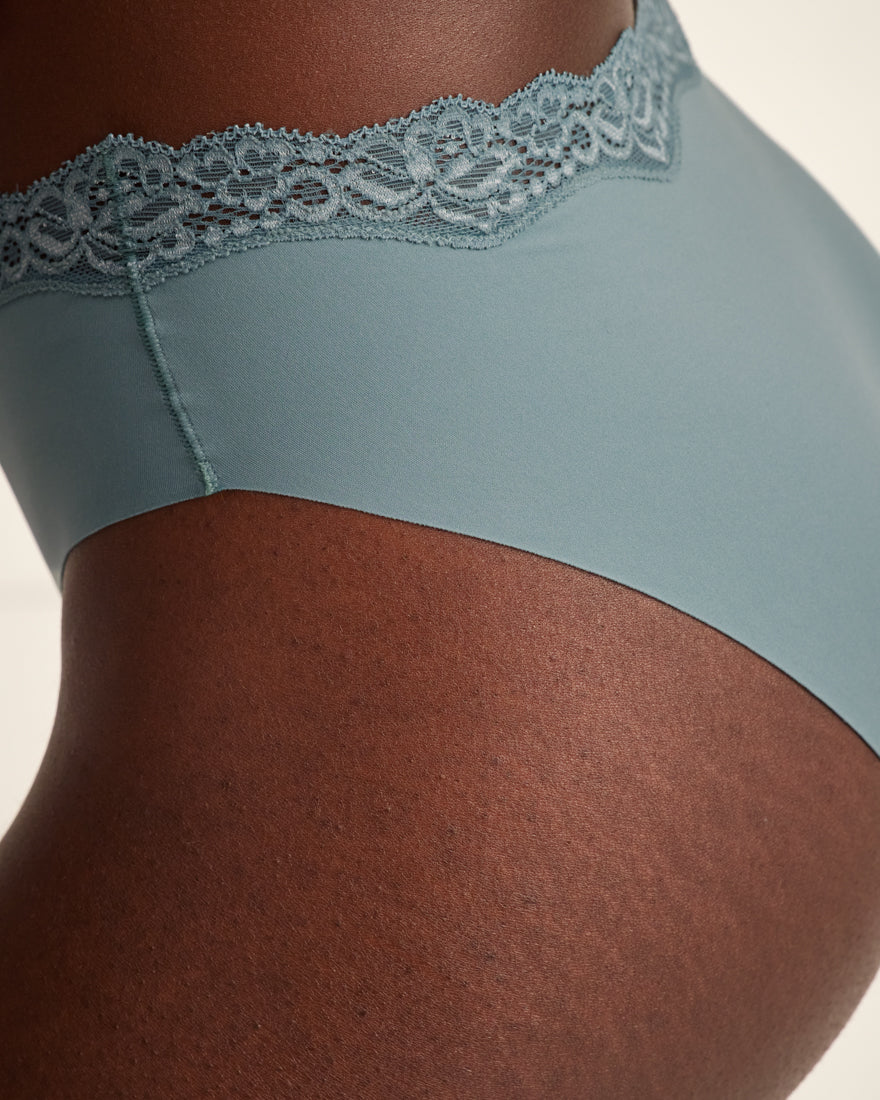 Modell trägt Periodenunterwäsche Slip Seamless Lace extra stark in blau mit nahtlosem Design mit Spitze am Bund.
Seitenansicht, Detail