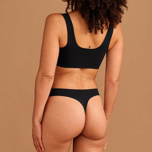 Modell trägt ooia Periodenunterwäsche String Seamless in Schwarz - nahtloser String mit leichter Saugstärke. Rückansicht.