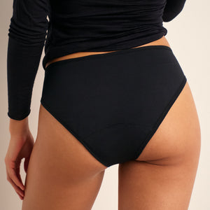 Modell trägt ooia Periodenunterwäsche Slip Comfy Cotton in schwarz aus Baumwolle.
hinten