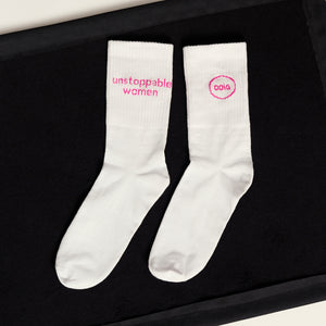 weiße ooia Socken mit dem pinken Aufdruck: Unstoppable Woman, liegen auf einer dunklen Fläche