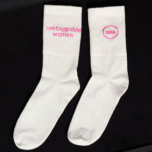 weiße ooia Socken mit dem pinken Aufdruck: Unstoppable Woman, liegen auf einer dunklen Fläche