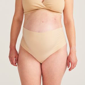 Modell trägt beigen moms Still BH und ooia The Belly Hugger Schwangerschafts-Panty in Beige mit hohem Bund