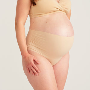 Modell trägt beigen moms Still BH und ooia The Belly Hugger Schwangerschafts-Panty in Beige mit hohem Bund