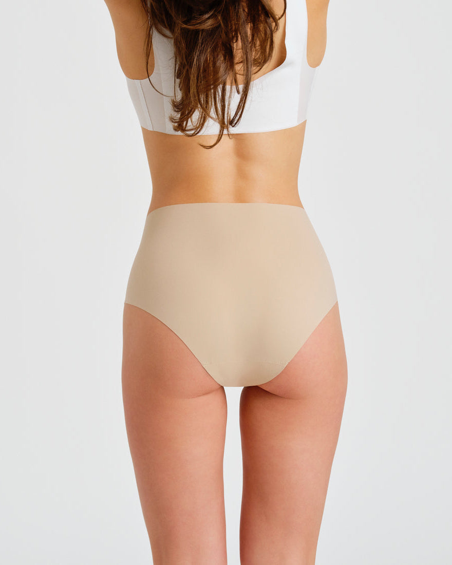 Modell trägt ooia everyday Highwaist Seamless in Beige – nahtlose Unterwäsche mit hohem Bund, die Slipeinlagen ersetzt. Rückansicht.