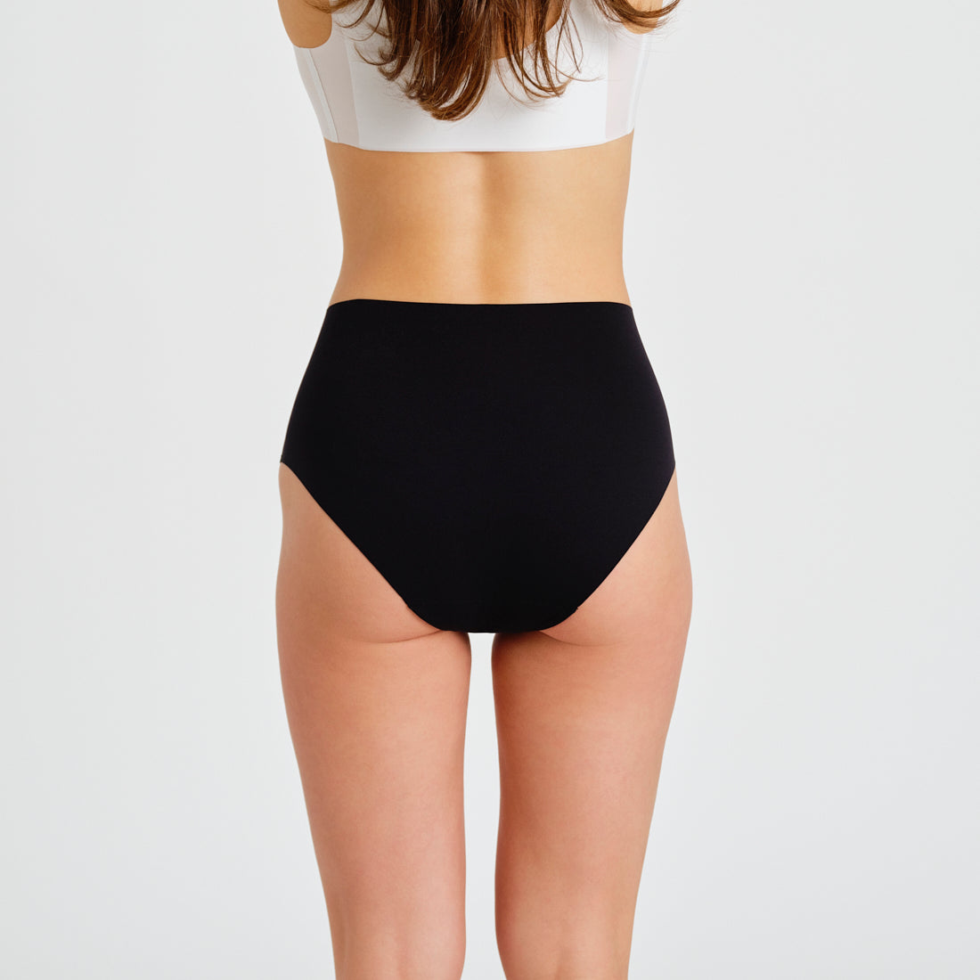 Modell trägt ooia everyday Highwaist Seamless in Schwarz – nahtlose Unterwäsche mit hohem Bund, die Slipeinlagen ersetzt. Rückansicht.