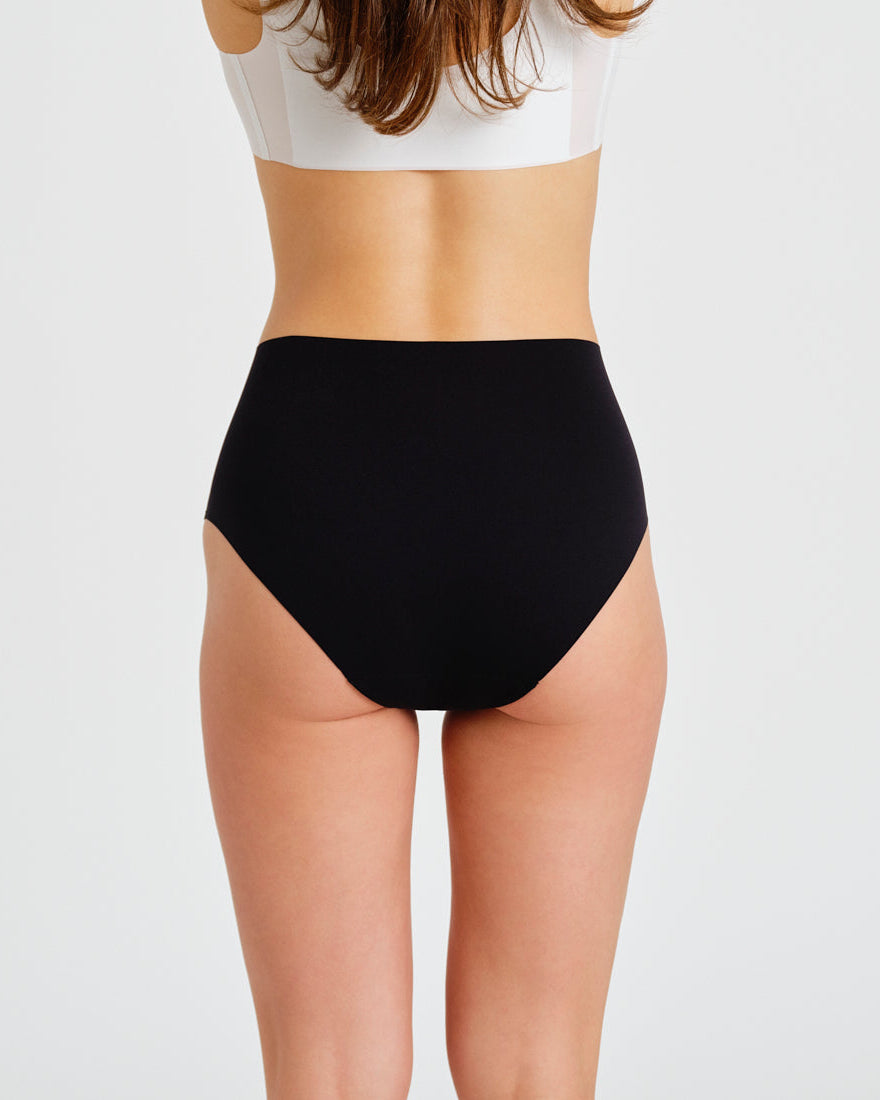 Modell trägt ooia everyday Highwaist Seamless in Schwarz – nahtlose Unterwäsche mit hohem Bund, die Slipeinlagen ersetzt. Rückansicht.