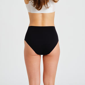 Modell trägt ooia everyday Highwaist Seamless in Schwarz – nahtlose Unterwäsche mit hohem Bund, die Slipeinlagen ersetzt. Rückansicht.